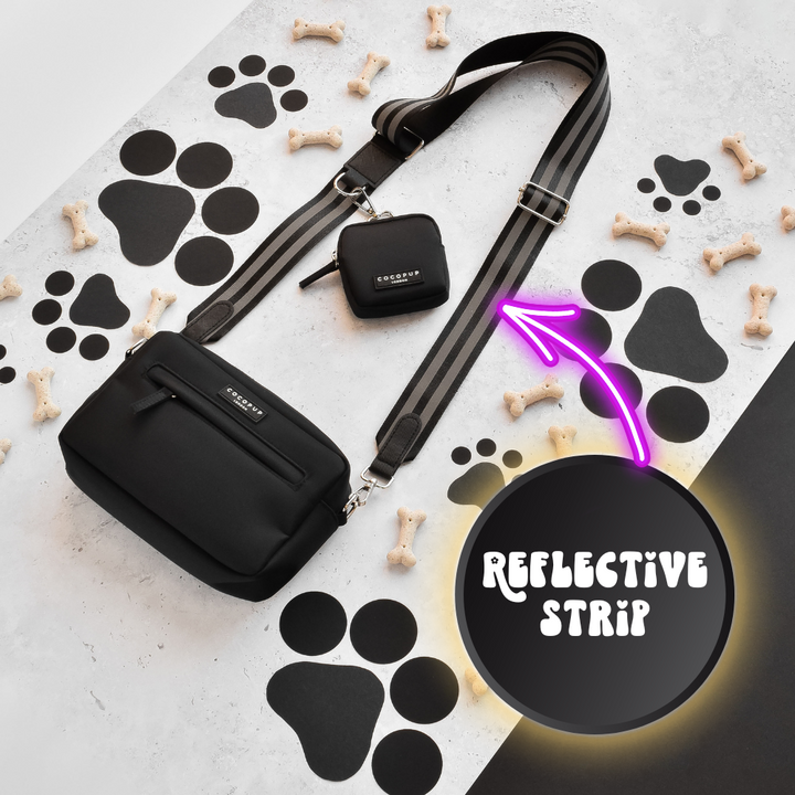 Introducing the Cocopup London Reflective Bag Strap in black, perfectly paired with a stylish crossbody bag adorned with paw print designs and scattered small bone-shaped treats. Ideal for late-night walks, this bag features a small attached pouch and is elegantly highlighted by a purple arrow on its reflective strap. The backdrop showcases a chic mix of black and white, accented by large paw prints.