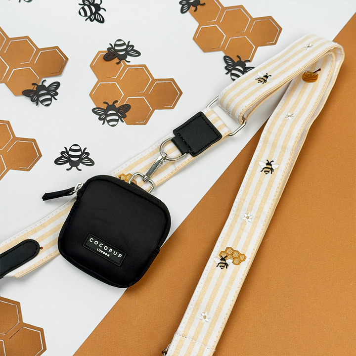 Pale yellow and white striped Bag Strap with bee and honeycomb embroidered decals. Attached is a Cocopup Treat Pouch in black.