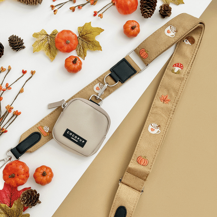 Brown bag strap, with attached treat pouch, with autumnal-themed embroidery of pumpkins, leaves, a coffee cup, and mushrooms.