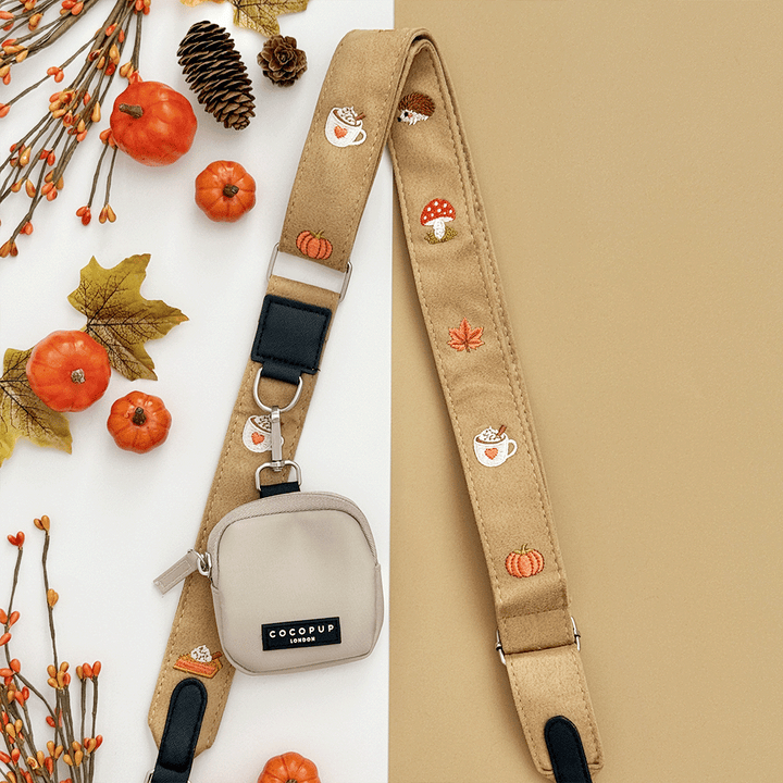Brown bag strap, with attached treat pouch, with autumnal-themed embroidery of pumpkins, leaves, a coffee cup, and mushrooms.