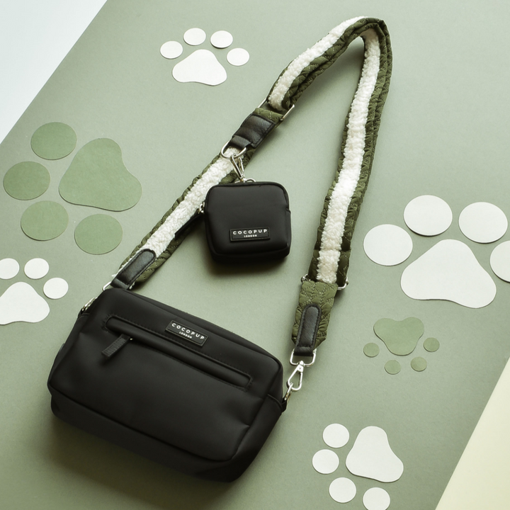 A Cocopup London Dog Walking Bag with khaki quilted straps and a matching small pouch is laid on a green background decorated with white paw prints. The bag and pouch feature brand labels reading "Cocopup London.