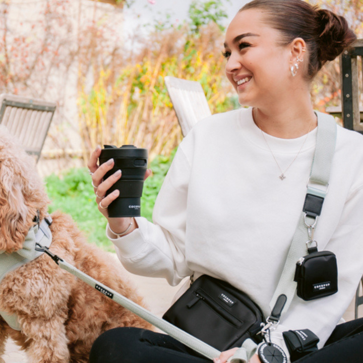 Model holding the Cocopup Black Coffee Cup whilst wearing the Cocopup Black Dog Walking Bag.